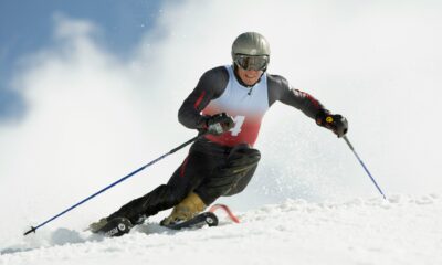 A skier carving down a snowy slope, wearing a helmet and goggles, with mountains in the background and powder flying up from their skis.