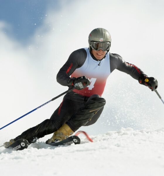 A skier carving down a snowy slope, wearing a helmet and goggles, with mountains in the background and powder flying up from their skis.