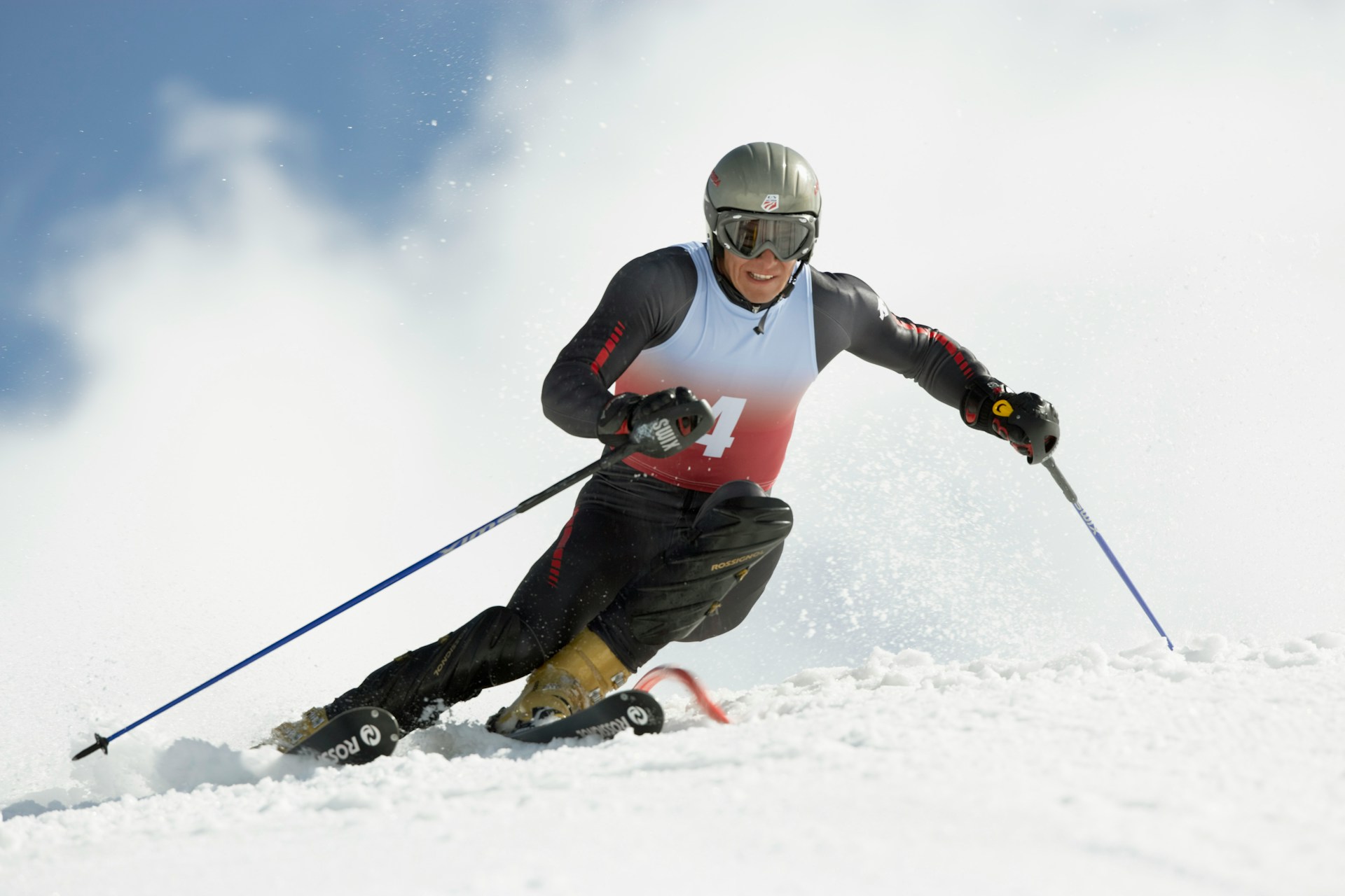 A skier carving down a snowy slope, wearing a helmet and goggles, with mountains in the background and powder flying up from their skis.